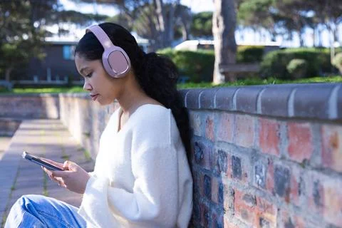 Child sitting on park path leaning on brick wall holding tablet wearing pink Stock Photos