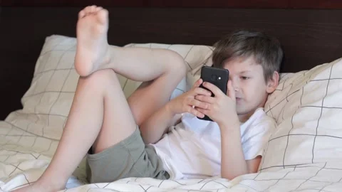 Child sitting relaxed in bed and playing on smartphone Stock Footage 160213522