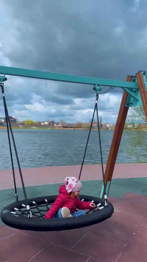 Child Sitting on Round Swing in Playground Near Water Stockbeeldmateriaal 333149555