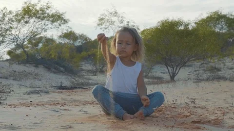 Child sitting on the sand at sunset warm light, pours sand in slow motion. Stock Footage 87900741