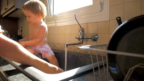 Child sitting in the sink while mother washing the dishes. Mother and daughter Stock Footage 121537449