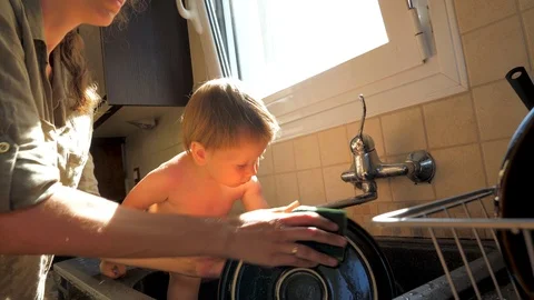 Child sitting in the sink while mother washing the dishes. Mother and daughter Stock Footage 122235387