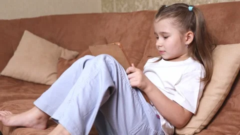 Child sitting on the sofa at home and holding a tablet in her hands Stock Footage 301016591