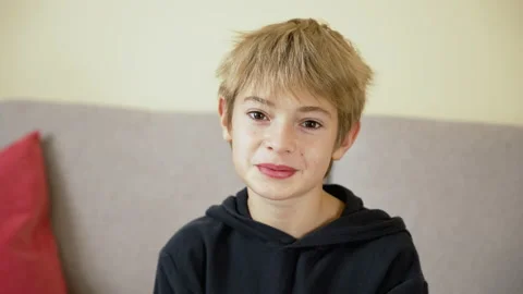 Child sitting on sofa at home, looking to camera, smiling, talking Stock Footage 239453320
