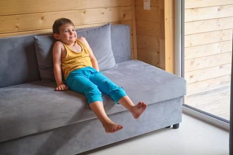Child sitting on soft grey sofa at home. Happy boy relaxing in living room wi 스톡 사진