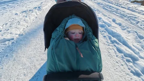 A child sitting in a stroller on a snowy winter day Stock Footage 329360775