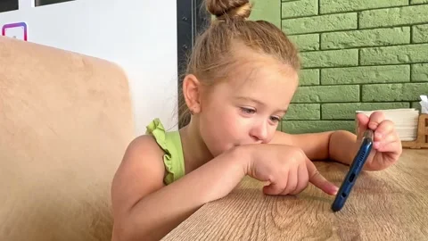 A child is sitting at a table in a cafe and playing games on the phone. Stock Footage 266163181
