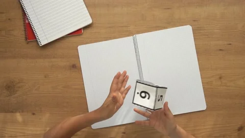 Child sitting at table with homework notebooks and playing game with paper dice Stock Footage 130861852