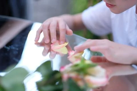 A child sitting at a table with a mirror surface and playing with rose petals Stock Photos