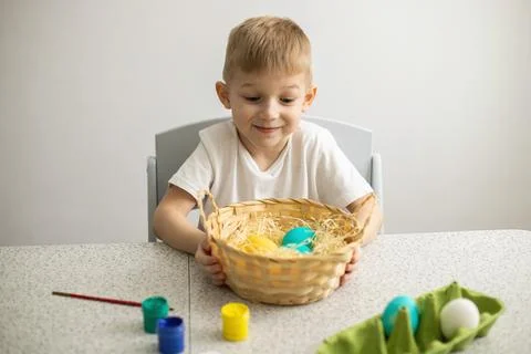 A child sitting at a table on a white background holds a wicker basket with p Stock Photos