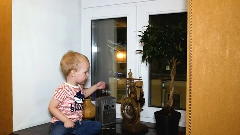 The child is sitting on the windowsill and playing with a vintage clock. Stock Footage 103091349