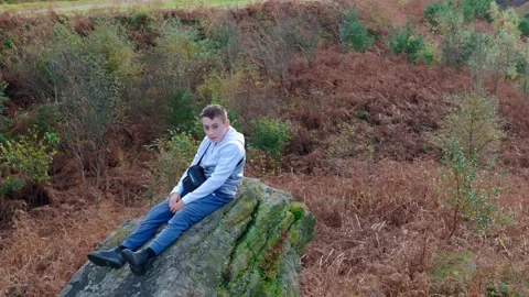 Child on sizable stone, deep in introspection. Aerial video revolves around.. 库存影片 254160014