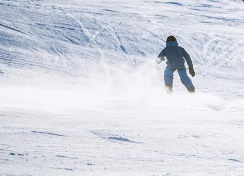 Child skiing down a steep alpine piste with snow spraying up behind him. Stock Photos