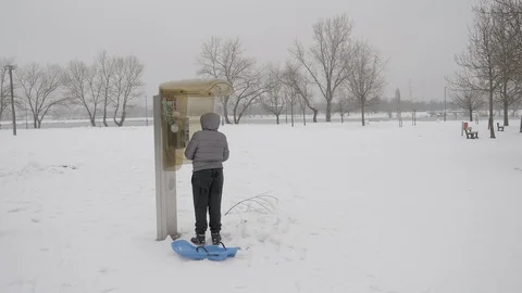 A child with sled using phone booth Stock Footage 87307813