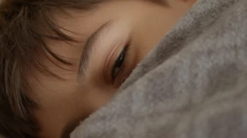 Child sleeps, eyes half-open, smiling softly under blanket Stock Footage 342191901