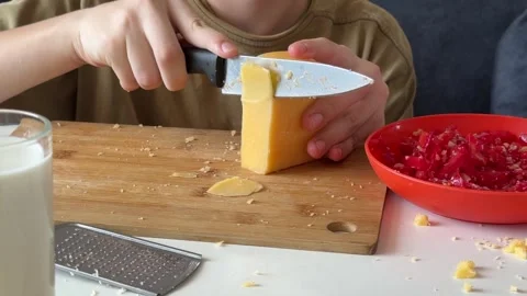 Child slicing block of cheese with knife, close-up hands, part of cheese and Stock Footage 337362339