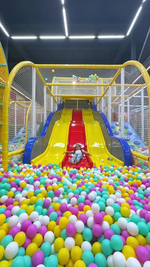 Child slides down from plastic colorful slide to dry pool with colorful balls. Stock Footage 304730455