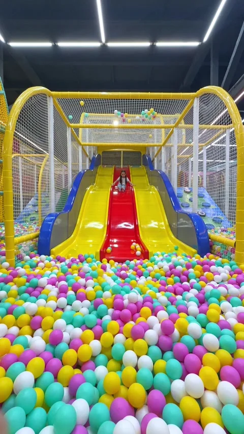 Child slides down from plastic colorful slide to dry pool with colorful balls. Stock Footage 304730461