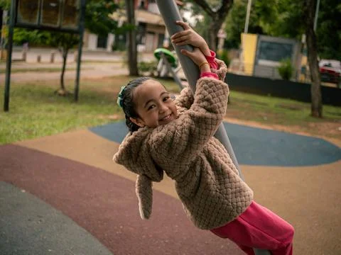 Child smiles while hanging on a playground pole Stock Photos