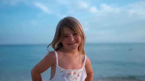Child smiling playfully by the beach under a clear sky Видео 341120132