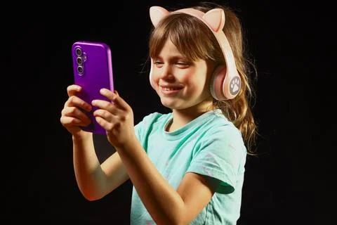 Child smiling while holding a smartphone and wearing headphones Stock Photos
