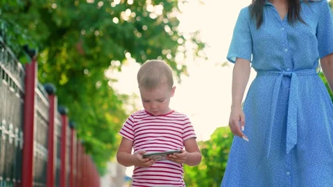 Child son uses smartphone while walking with mother outdoors summer. Happy Stock Footage 336749542