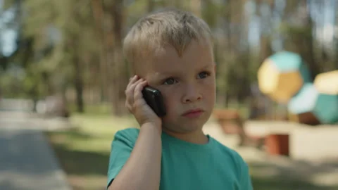 Child speaking by a cellular phone device in a park. Stock-Footage 343208732
