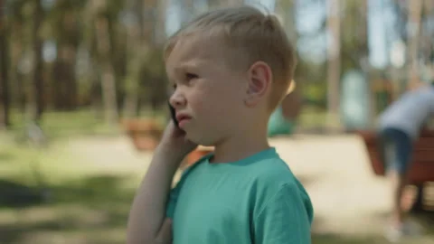 Child speaking by a cellular phone device in a park. 動画素材 343208843