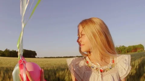 Child spinning with balloons at wheat field . Girl looking at camera. Lens flare Stock Footage