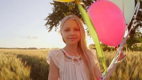 Child spinning with balloons at wheat field . Girl looking at camera. Lens flare Stock Footage 80551999