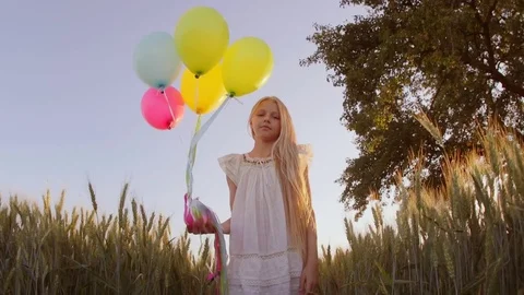 Child spinning with balloons at wheat field . Girl looking at camera. Lens flare Stock-Footage 80552155