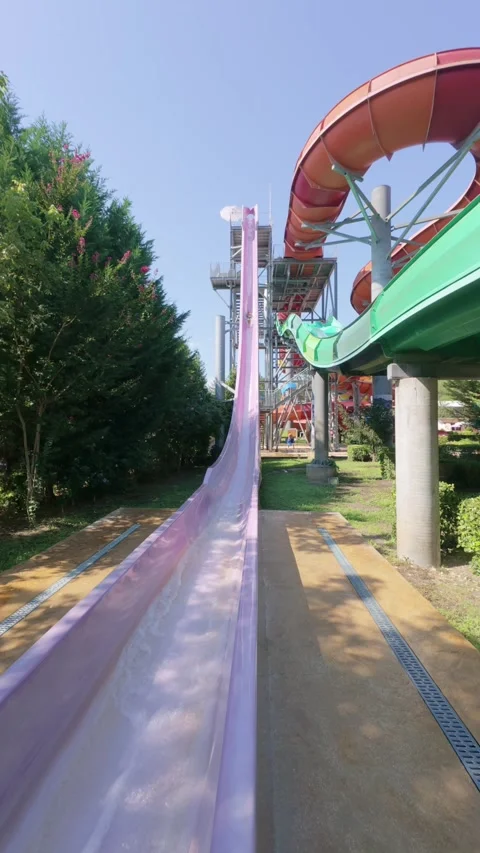 Child splashing down from a tall, vertical water slide at a water park on a Stock Footage 316399048