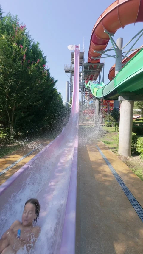 Child splashing down from a tall, vertical water slide at a water park on a Stock Footage 316399151