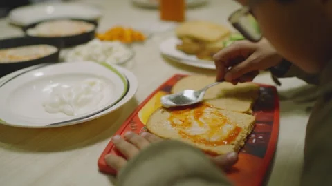 Child spreading marmalade over bread with spoon. Special children's school Stock Footage 333374595