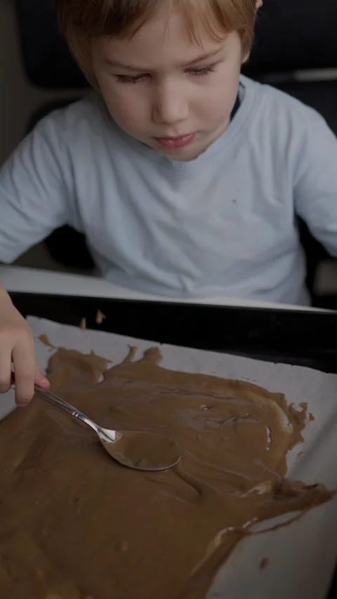 Child spreading melted chocolate on baking sheet Stock Footage 327011181