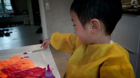 Child squeezing paint from a bottle and brushing it onto the paper Stock Footage 219107560