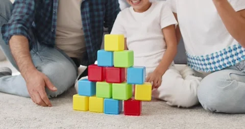 Child stacking colorful toy blocks into a small pyramid while parents watch Stock Footage 325828508