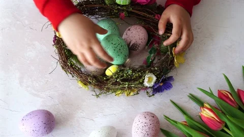 Child stacks colorful eggs in an easter wreath. Easter DIY and creativity Stock Footage 236453140