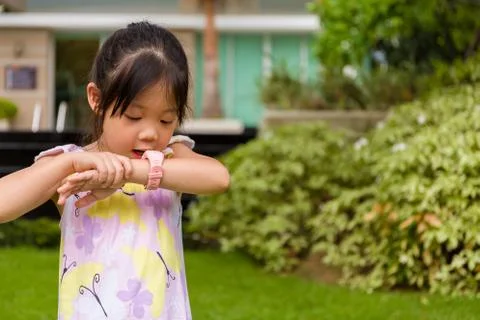 Child standing in garden using smartwatch or smart watch on her wrist. Stock Photos