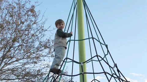Child standing on rope net at park showing playground adventure and physical Video stock 329278891