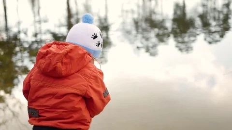 A child stands on the Bank of the pond and throwing stones. Walks in the fresh Stock Footage