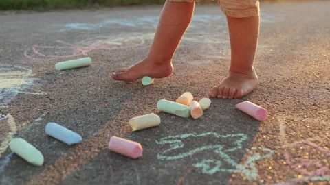 A child stands barefoot on the sidewalk surrounded by colorful chalk pieces. Stock Footage 340960513
