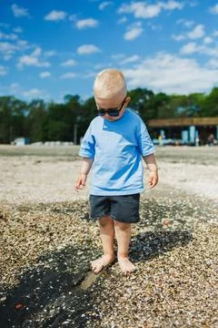 Child stands on beach looking down at the ground while wearing sunglasses a.. Stock Photos