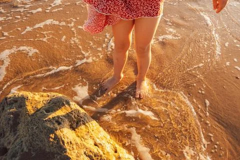 Child stands on beach at sunset, feeling water wash over feet while enjoying  Stock Photos