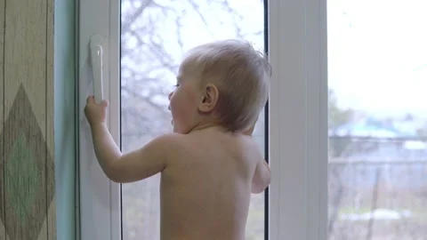 The child stands in front of the window and knocks on the glass with his palm Stock Footage 142376006