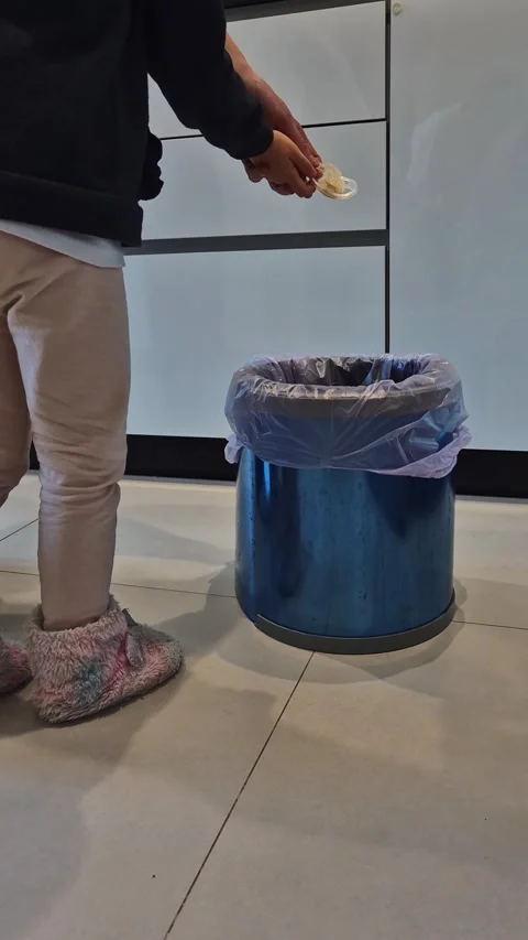 A child stands in a kitchen, dropping a damaged pacifier into the trash 库存影片 301329876