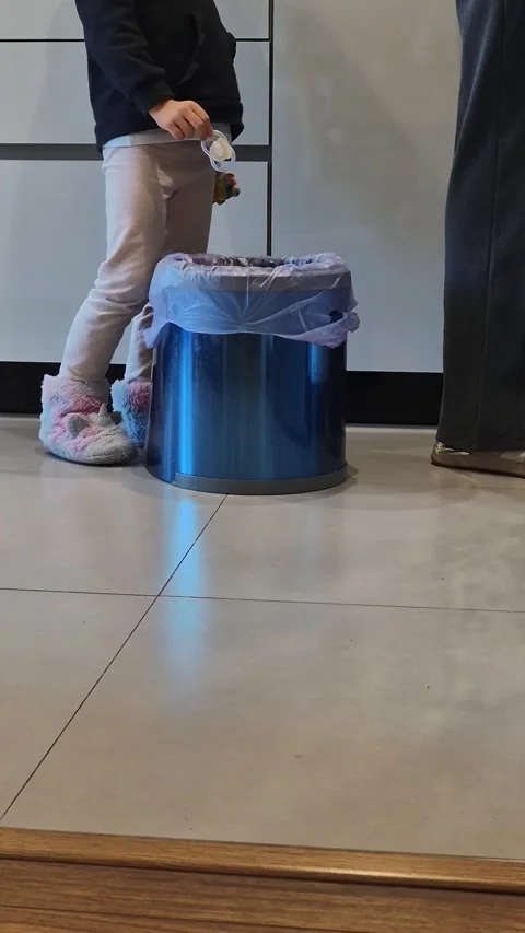 A child stands in a kitchen, dropping a damaged pacifier into the trash 库存影片 301329878