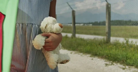 Child stands outside holding a stuffed bear while walking along a dirt path in Stock Footage 327444625