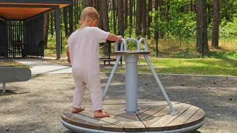 A child stands on a spinning platform in a park. The child holds a green object Stock Footage 339031042