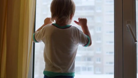 A child stands on the windowsill and looking out the window Vidéo 70375851